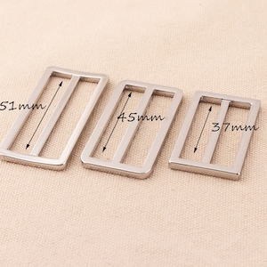 Könnte beinhalten: Drei silberfarbene, rechteckige Metallschieber mit abgerundeten Kanten. Der größte misst 5,1 cm in der Länge, der mittlere 4,5 cm und der kleinste 3,7 cm. Sie haben zwei parallele Stäbe im Inneren.