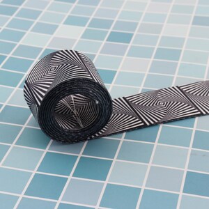 May include: Black and white patterned ribbon rolled up on a blue tiled surface. The pattern is a series of concentric squares.