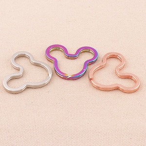 May include: Three metal keychains in the shape of a Mickey Mouse head. The keychains are silver, rainbow, and rose gold.
