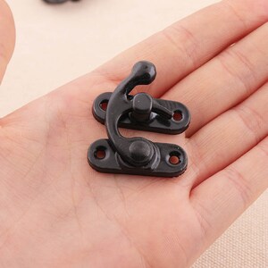 May include: Black metal clasp with a hook and two holes. The clasp is designed to be used for fastening two pieces of fabric together.