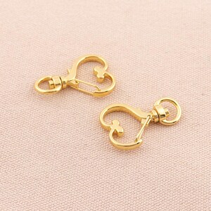 May include: Two gold-toned heart-shaped keychains with a spring clasp and a swivel hook.