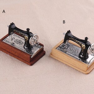 May include: Two miniature black sewing machines with gold accents on wooden bases. The sewing machine on the left has a dark brown base, while the sewing machine on the right has a light brown base.