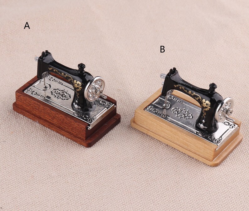 May include: Two miniature black sewing machines with gold accents on wooden bases. The sewing machine on the left has a dark brown base, while the sewing machine on the right has a light brown base.