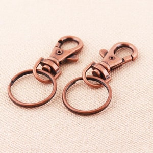 Pode incluir: Dois chaveiros de cor cobre com um fecho giratório e um anel redondo.