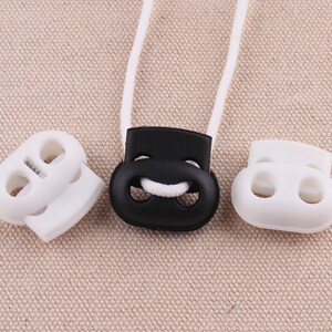 May include: Three plastic cord locks, two white and one black. The white cord locks have two holes each, while the black cord lock has a single hole.