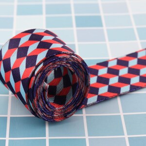 K&ouml;nnte beinhalten: Ein rot-blau-wei&szlig;es Band mit geometrischem Muster. Das Band ist aufgerollt und das Muster ist auf beiden Seiten sichtbar.