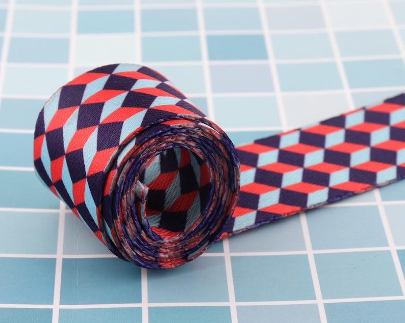 K&ouml;nnte beinhalten: Ein rot-blau-wei&szlig;es Band mit geometrischem Muster. Das Band ist aufgerollt und das Muster ist auf beiden Seiten sichtbar.