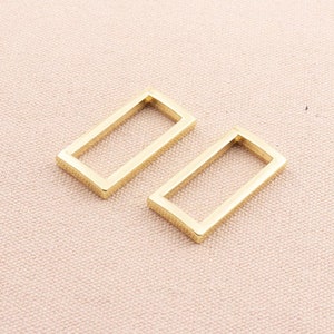 May include: Two gold-colored metal rectangular hoops. The hoops are open on one side and have a smooth, polished finish.
