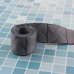 May include: Black and white patterned ribbon with a swirling, optical illusion design. The ribbon is rolled up and the pattern is visible on both sides.