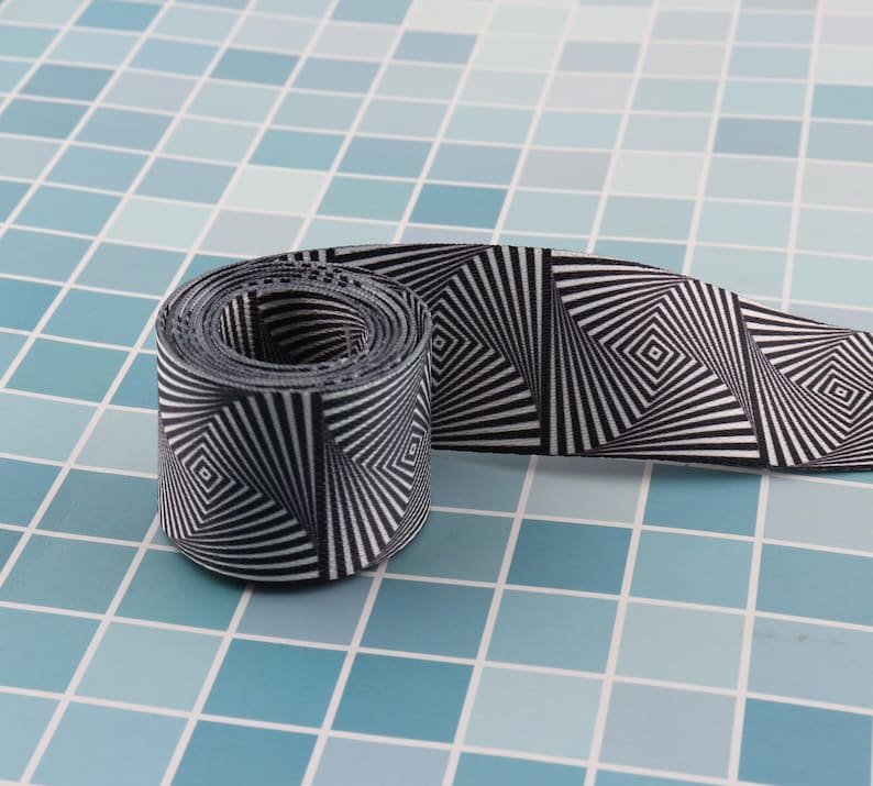 May include: Black and white patterned ribbon with a swirling, optical illusion design. The ribbon is rolled up and the pattern is visible on both sides.