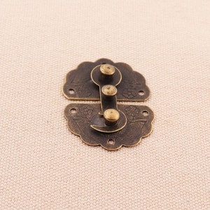 May include: Antique brass latch with a floral design and three round knobs. The latch is made of metal and has a decorative finish.