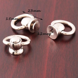 Könnte beinhalten: Drei silberne Metallringe mit einem Schraubsockel. Die Ringe haben einen Durchmesser von 15 mm und der Sockel einen Durchmesser von 12 mm. Die Ringe sind 23 mm lang.