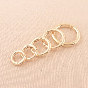 May include: Five gold-toned metal key rings of different sizes, arranged in a row from largest to smallest.