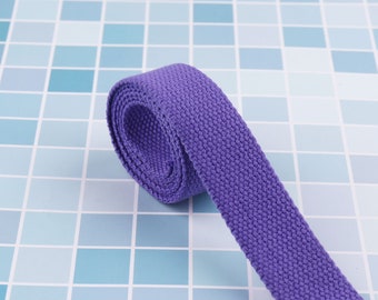 May include: A close-up of a purple cotton webbing strap rolled up on a blue tiled surface.