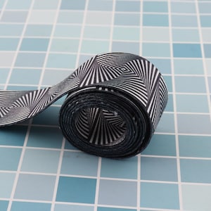 May include: A black and white patterned elastic band rolled up on a blue tiled surface. The pattern is a series of concentric circles with a diamond shape in the center.
