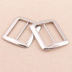 May include: Two silver-toned metal slider buckles. The buckles are rectangular with rounded corners and have a smooth, polished finish.