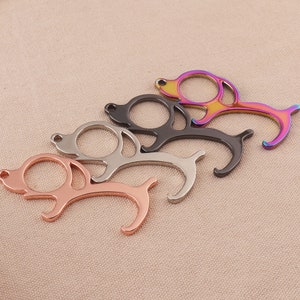 Puede incluir: Cuatro abridores de puertas con forma de perro en diferentes colores: oro rosa, plata, negro e iridiscente. Los abridores tienen un bucle en la parte superior para sujetarlos a un llavero.