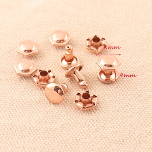 May include: A set of rose gold metal rivets, some with a post and some without. The rivets are 8 mm in diameter and 9 mm in height.