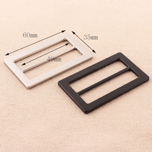 May include: Two metal belt buckle sliders, one silver and one black. The silver slider measures 60mm by 49mm and the black slider measures 35mm by 49mm.