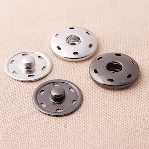 May include: Four metal snap buttons, two silver and two black, with a raised center post and a ring of small holes around the edge.