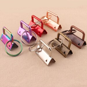 May include: Set of six metal key rings in various colors, including silver, gold, red, purple, and bronze. Each ring has a rectangular shape with a small triangular opening at the top.