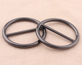 May include: Two black metal rings with a bar across the center. The rings are interlocked and have a smooth, polished finish.
