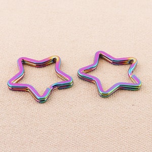 May include: Two iridescent rainbow star-shaped keychains. The keychains are made of metal and have a smooth, shiny finish.
