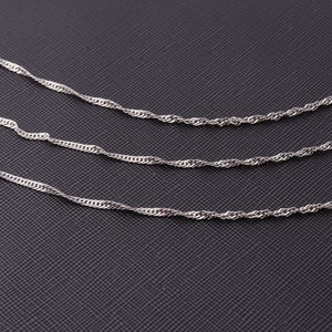 Può includere: Tre catene in corda d'argento di diverse lunghezze su uno sfondo nero testurizzato.