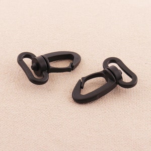 Puede incluir: Dos ganchos giratorios de plástico negro. Los ganchos tienen una forma ovalada redondeada con un pequeño pivote redondo en el centro.