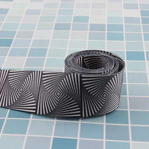 May include: A black and white patterned ribbon with a swirling, optical illusion design. The ribbon is rolled up and is on a blue tiled surface.