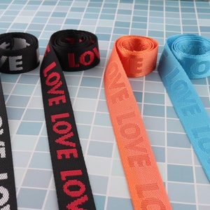 May include: Four different colors of woven webbing with the word "LOVE" repeated in red on each strap. The straps are black, orange, blue, and white.