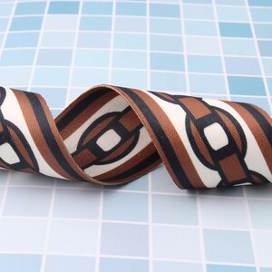 May include: Brown and white striped ribbon with a chain link pattern. The ribbon is curled and has a textured surface.