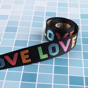 May include: Black woven webbing with the word "LOVE" repeated in colorful embroidered letters. The webbing is rolled up and the letters are visible on both sides.
