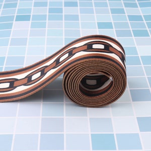 May include: Brown and white patterned ribbon with a chain link design. The ribbon is rolled up and the pattern is visible on the outside of the roll.