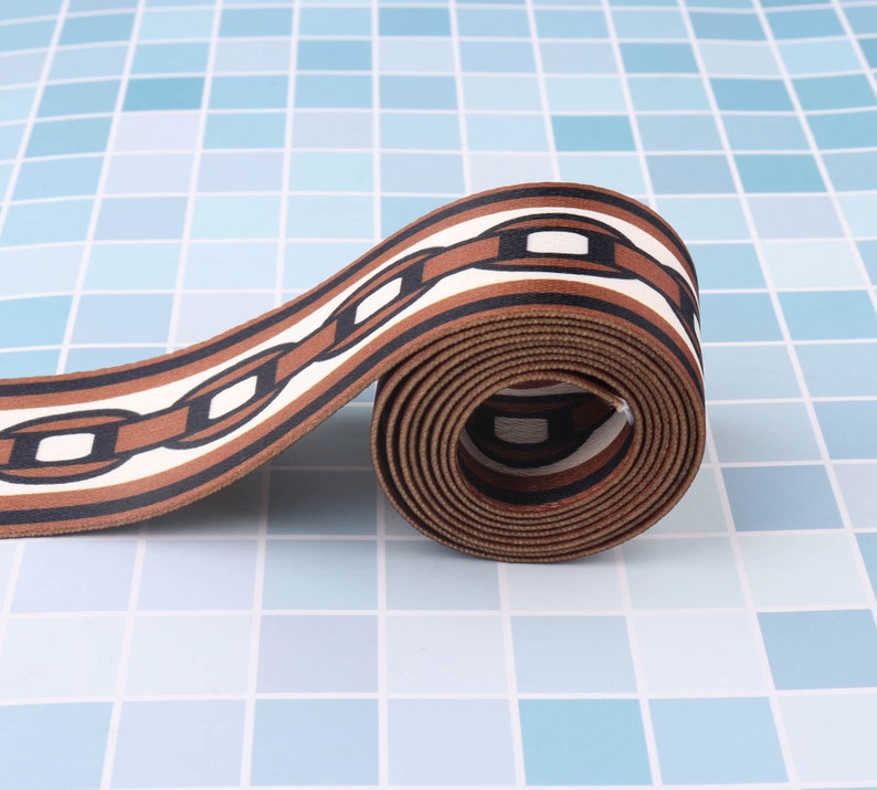 May include: Brown and white patterned ribbon with a chain link design. The ribbon is rolled up and the pattern is visible on the outside of the roll.
