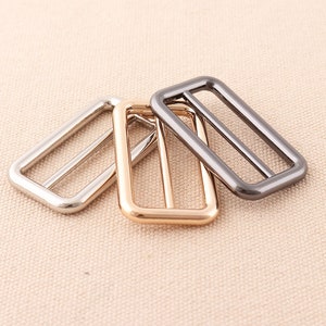May include: Three metal rectangular belt buckle slides in silver, gold, and black.