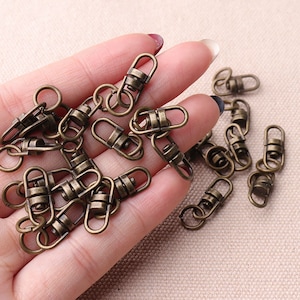 May include: A close-up of a hand holding a pile of antique gold-toned metal swivel clasps. The clasps are small and have a simple design.