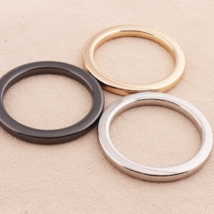 May include: Three metal rings in different finishes: black, silver, and gold. The rings are all the same size and are arranged in a circle.