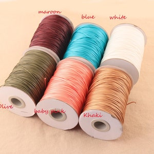 May include: Six spools of waxed cotton cord in various colors, including olive, baby pink, khaki, maroon, blue, and white. The spools are labeled with the color names.