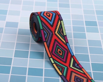 Puede incluir: Una cinta tejida colorida con un patrón geométrico en tonos de rojo, naranja, amarillo, verde, azul, morado y negro. La cinta está sobre una superficie de azulejos azules.