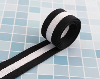 May include: Black and white striped webbing with a white stripe down the center. The webbing is rolled up and the end is laying flat.