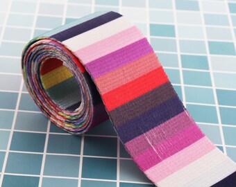 Puede incluir: Una cinta de tela rayada multicolor enrollada con una variedad de colores, incluyendo rosa, rojo, azul y blanco.