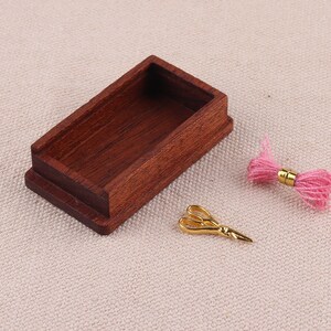 May include: A miniature wooden box with a lid, a pair of gold scissors, and a pink ball of yarn.