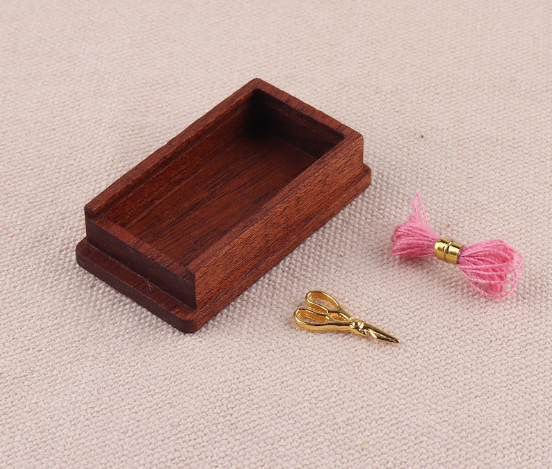 May include: A miniature wooden box with a lid, a pair of gold scissors, and a pink ball of yarn.