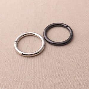 May include: Two metal rings, one silver and one black, with a snap closure. The rings are on a beige fabric background.