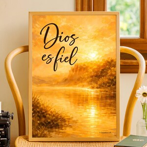 May include: A framed art print with a warm, golden landscape painting. The artwork depicts a sunset over a body of water, with the words "Dios es fiel" in elegant script. The print is in a light wood frame.