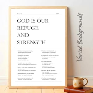 May include: A framed print with the text "GOD IS OUR REFUGE AND STRENGTH" from Psalm 46. The print is in black and white, with a wooden frame. A small mug and a book are on a wooden surface.
