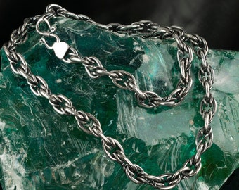 May include: A silver chain necklace with a twisted rope design, displayed on a green glass rock.