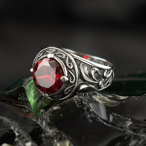 May include: A silver ring with an ornate design and a large, red gemstone.