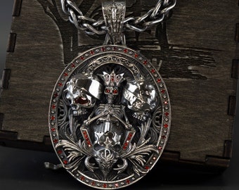 May include: A silver pendant necklace with a detailed design featuring three skulls, a skeleton holding a sword, and red gemstones. The pendant is surrounded by a decorative border.